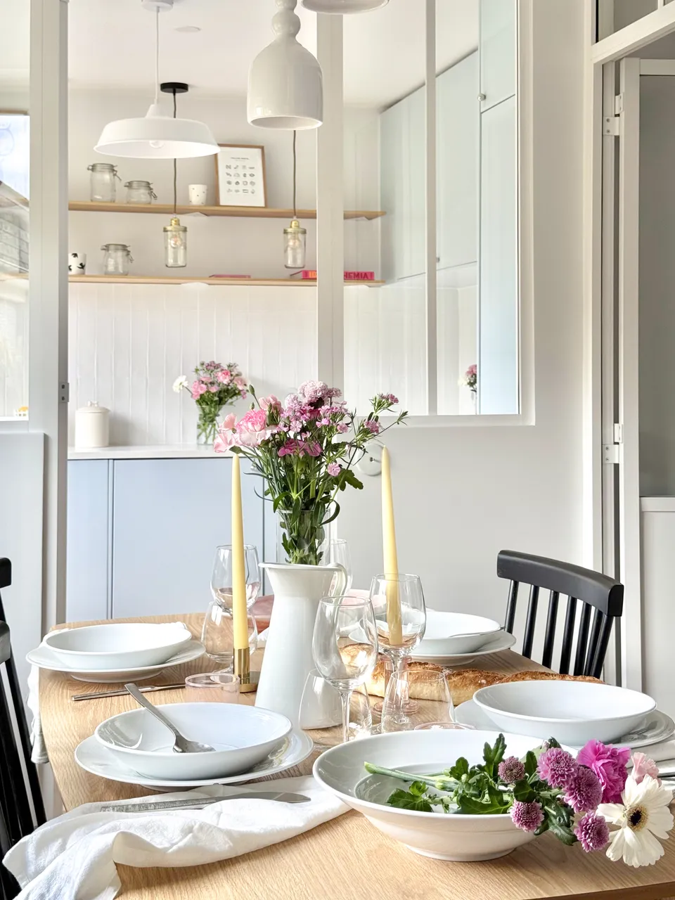 Studio Madame : architecte d’intérieur, Paris et Montmorency
Projet réalisé à Montmorency.
Photographie d’intérieur : salle à manger avec vue sur cuisine, composée d’une table rectangulaire avec 4 chaises vintages noires. La table est dressée et des suspensions tombent au-dessus de la table. La cuisine de couleur bleu ciel est visible en transparence grâce à la verrière atelier séparant les deux espaces.
