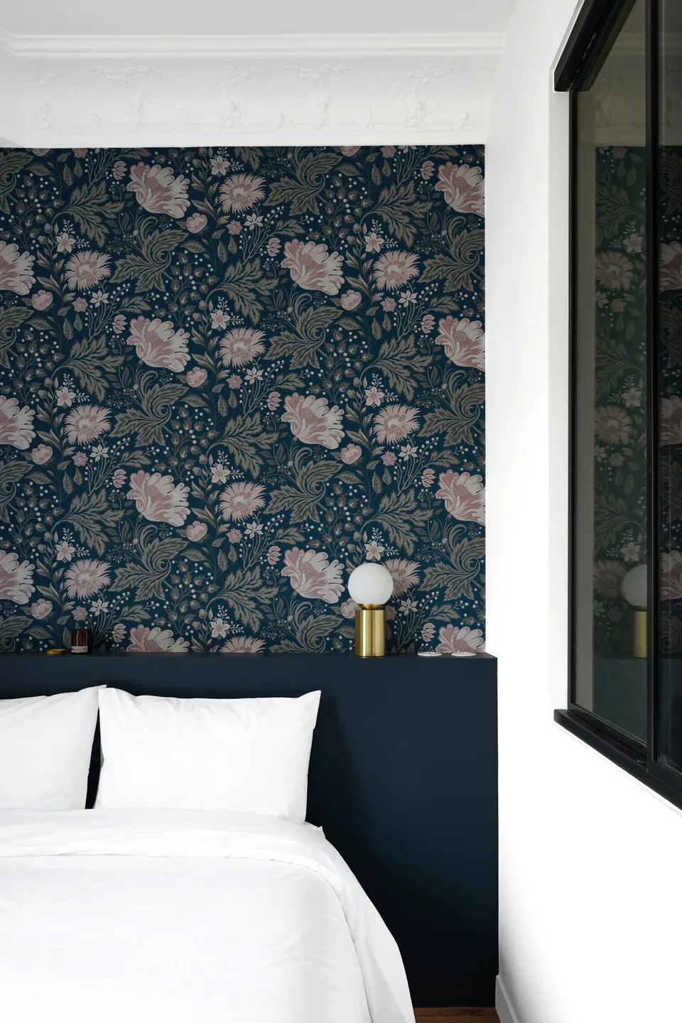 Studio Madame : architecte d’intérieur, Paris et Montmorency.
Projet réalisé à Boulogne-Billancourt. 
Photographie d’intérieur : chambre (vue sur coin nuit) peinte en blanc et bleu foncé (Ressource) et habillée d’un papier peint fleuri dans des tons de bleu et de rose.
Côté déco, le lit est recouvert d’une parure blanche et une lampe de chevet dorée est posée sur la tête de lit.
Les autres murs sont peints en blanc (Ressource) et un parquet massif ancien est au sol.