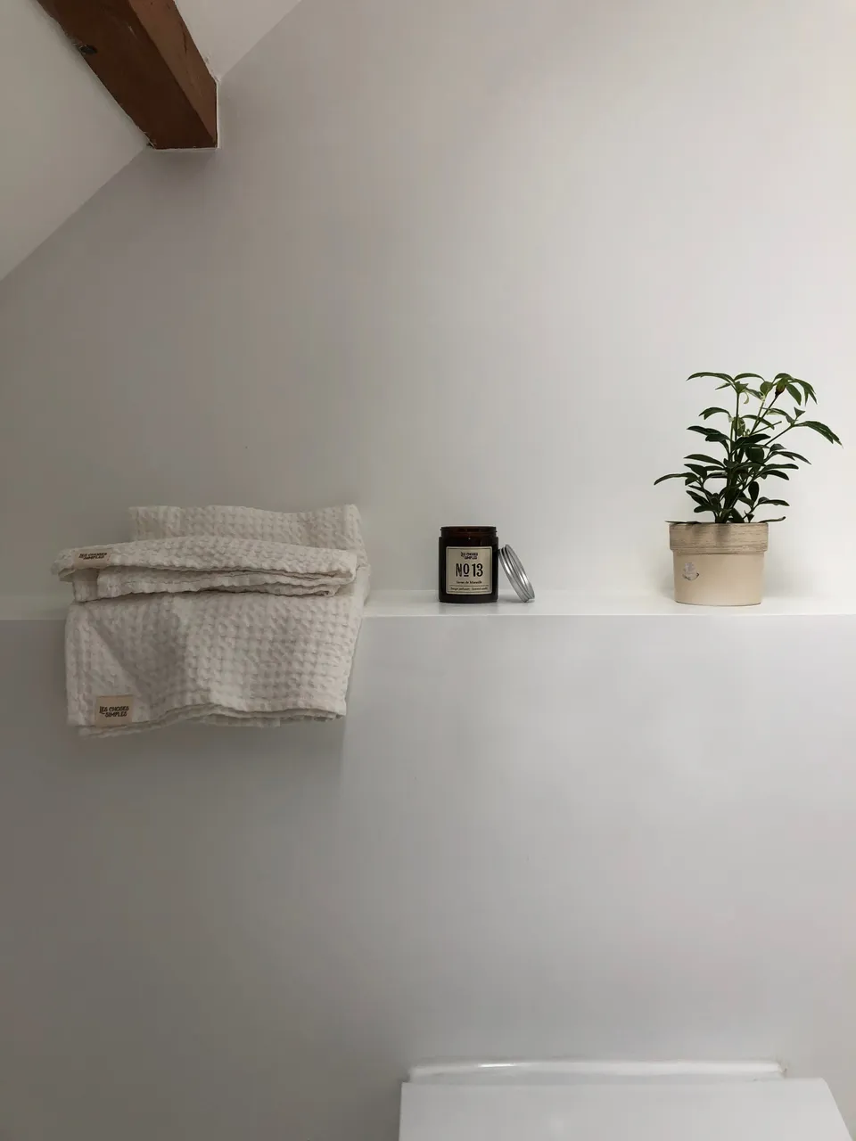 Studio Madame : architecte d’intérieur, Paris et Montmorency
Projet réalisé à Saint-Gratien.
Photographie d’intérieur : salle de bain sous pente avec coffrage réalisé dans l’alignement du meuble vasque, sur lequel repose une plante, une bougie et des draps de bain.