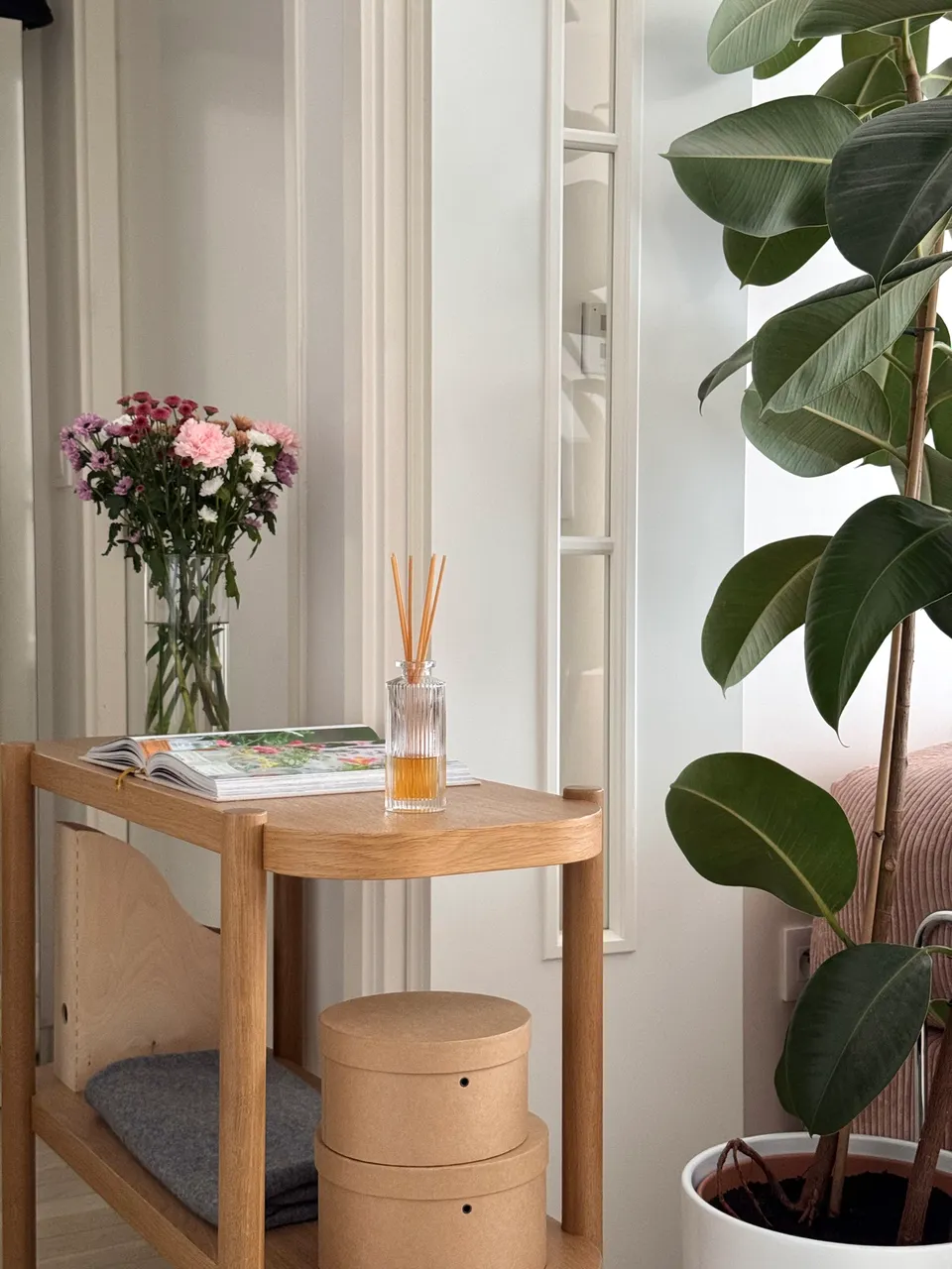 Studio Madame : architecte d’intérieur, Paris et Montmorency
Projet réalisé à Montmorency.
Photographie d’intérieur : entrée vers le salon, composée d’une console en chêne sur laquelle reposent un livre, un bouquet de fleurs et un diffuseur. Une grande plante verte sépare l’entrée d’un canapé rose.