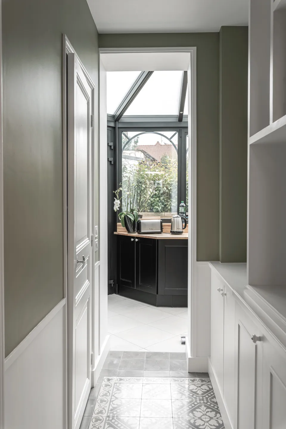 Studio Madame : architecte d’intérieur, Paris et Montmorency
Projet réalisé à Enghien-les-Bains.
Photographie d’intérieur : couloir de type haussmannien, composé de soubassements blancs et de murs peints en kaki en partie haute et donnant sur la cuisine, nichée sous une verrière art déco.