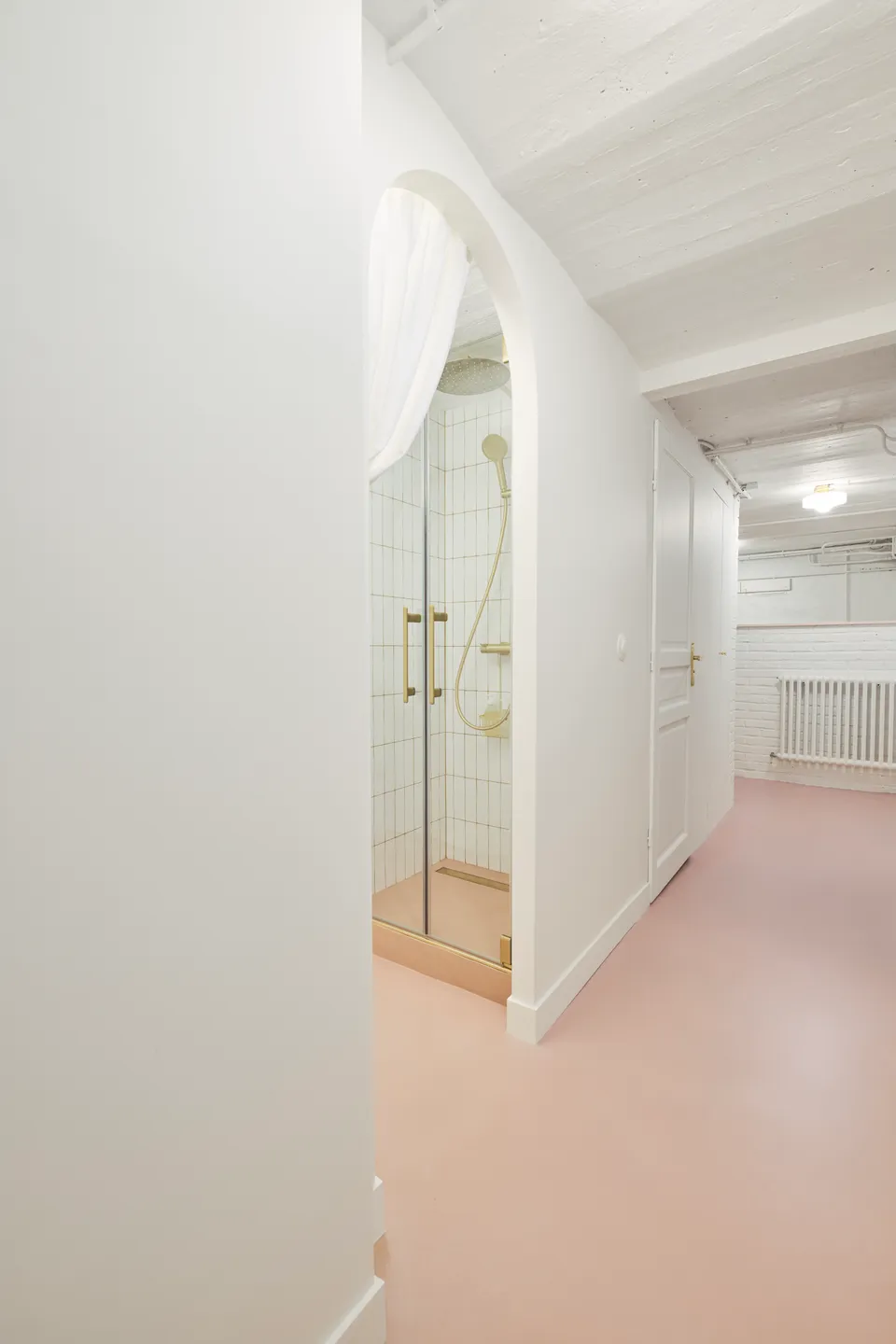Studio Madame : architecte d’intérieur, Paris et Montmorency.
Projet réalisé à Deuil-la-Barre.
Photographie d’intérieur : couloir entièrement repeint en blanc (Ressource) amenant sur une petite salle de bain par un passage en arche habillé d’un rideau blanc. Le sous-sol présente toutes les caractéristiques typiques d’une meulière (plafond voûté, tuyaux apparents, briques, etc.). Les murs sont peints en blanc (Ressource) et le sol est habillé d’un béton ciré rose (Harmony Béton).