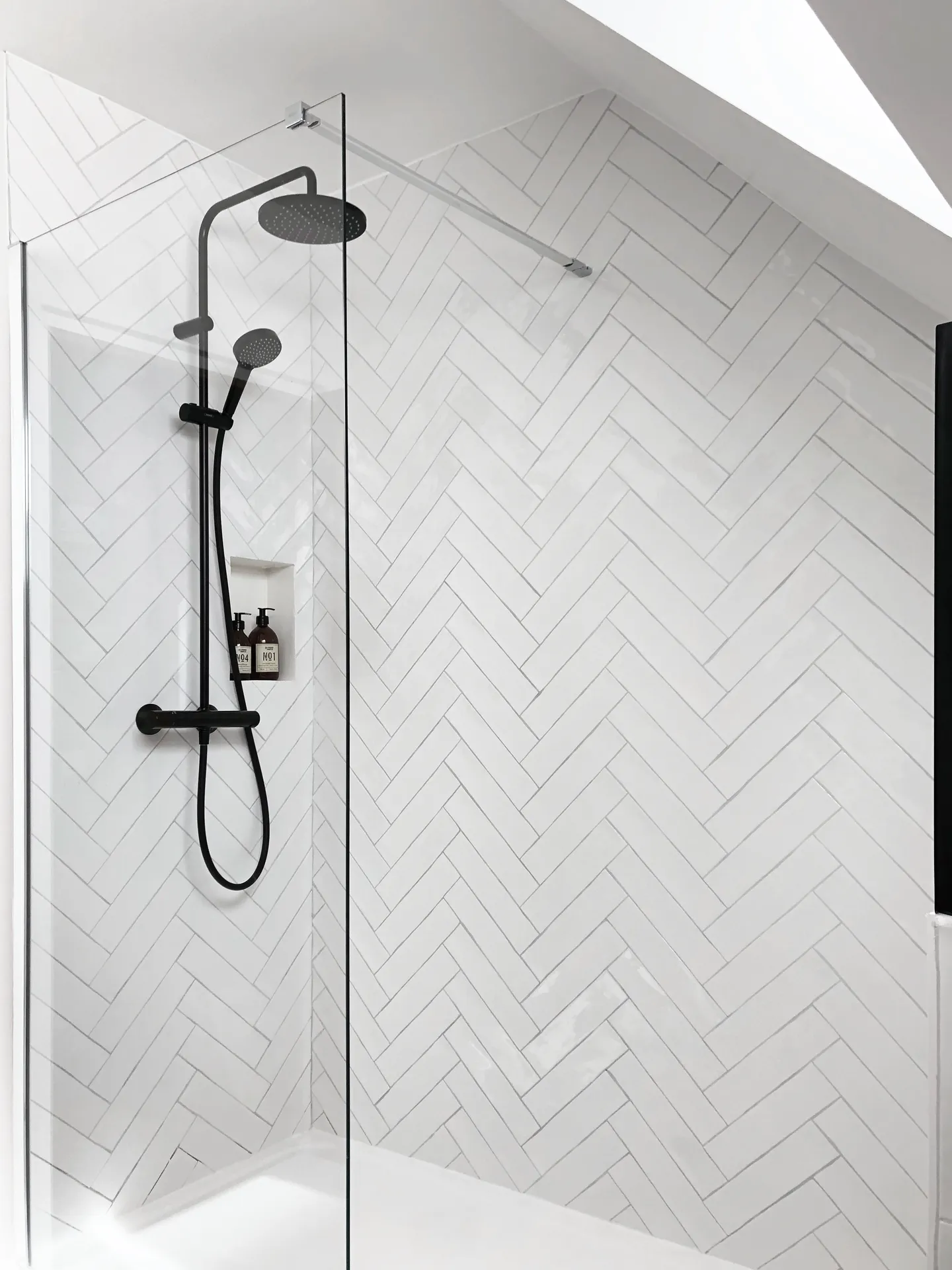 Studio Madame : architecte d’intérieur, Paris et Montmorency
Projet réalisé à Saint-Gratien.
Photographie d’intérieur : salle de bain sous pente avec douche séparée par une paroi en verre, faïence blanche artisanale pour la crédence (pose en chevron), robinetterie noire et niche rectangle.