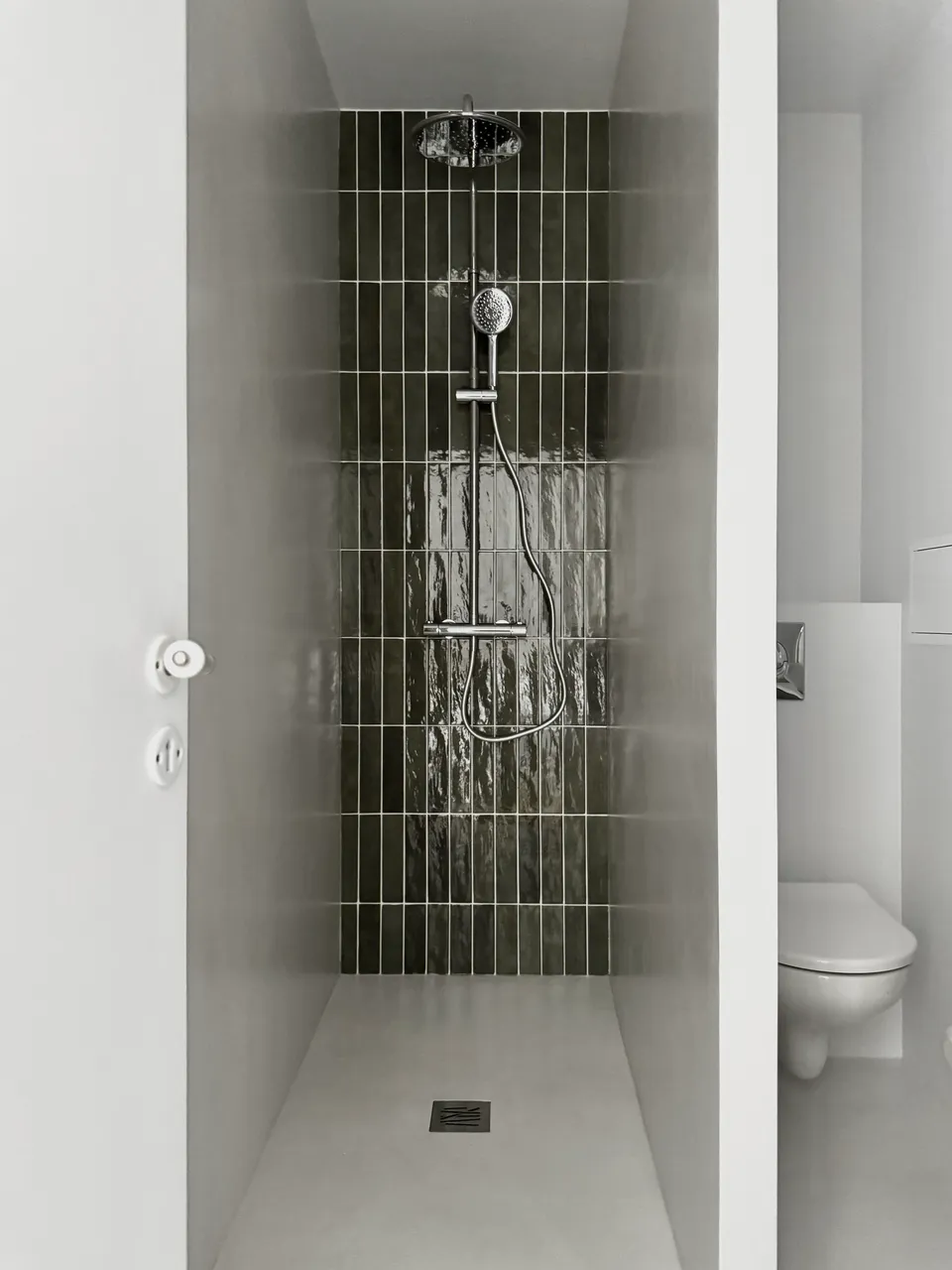 Studio Madame : architecte d’intérieur, Paris et Montmorency
Projet réalisé à Montmorency.
Photographie d’intérieur : salle de bain composée d’une grande douche avec robinetterie chromée et revêtue d’une faïence artisanale verte sur l’un des murs et d’un béton ciré gris clair au sol et sur les autres murs.