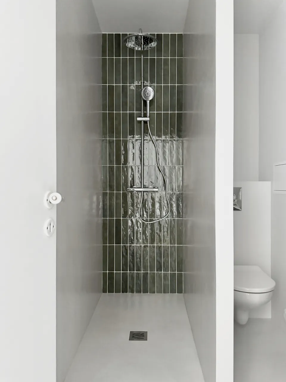 Studio Madame : architecte d’intérieur, Paris et Montmorency
Projet réalisé à Montmorency.
Photographie d’intérieur : salle de bain composée d’une grande douche avec robinetterie chromée et revêtue d’une faïence artisanale verte sur l’un des murs et d’un béton ciré gris clair au sol et sur les autres murs.