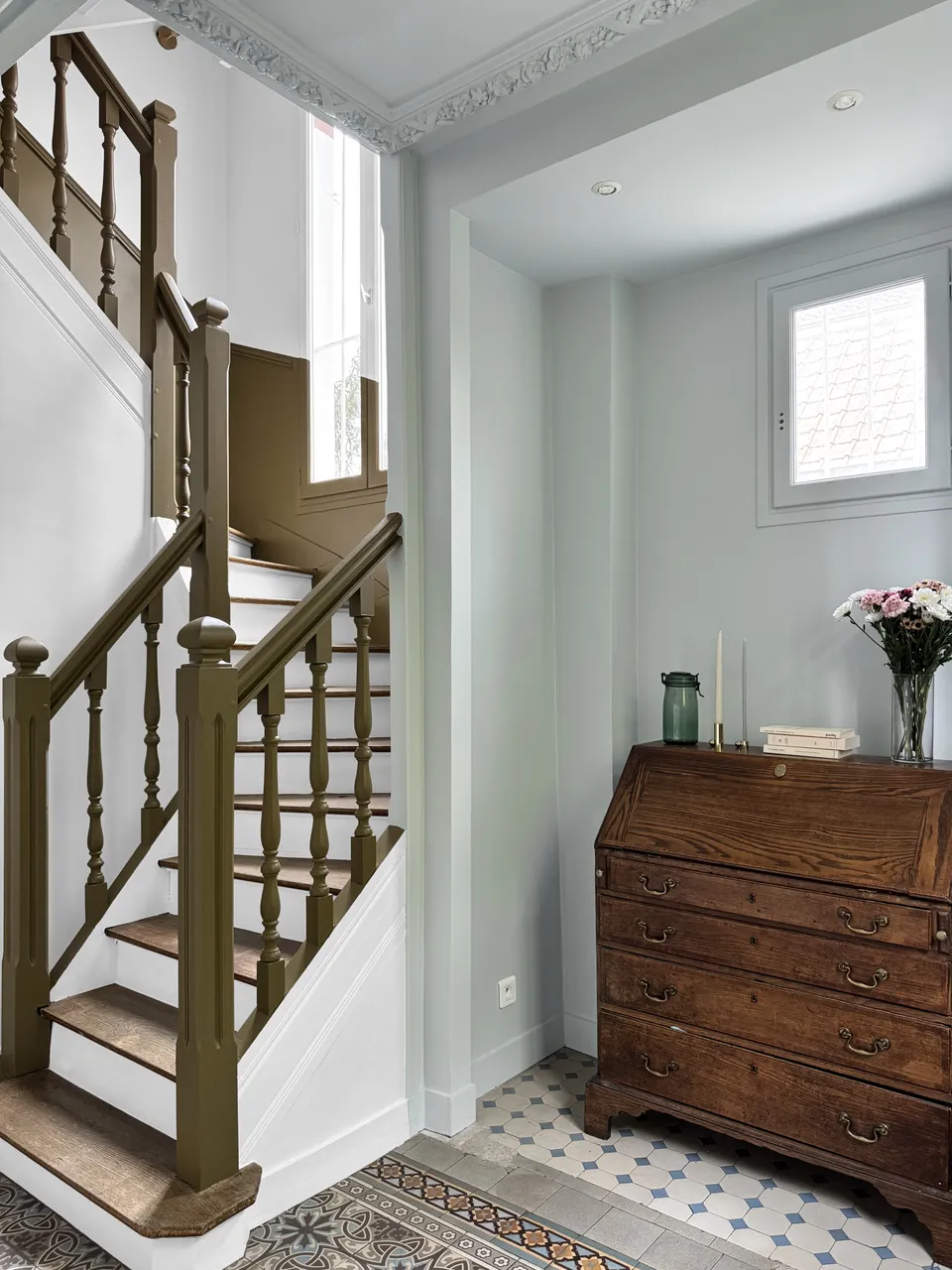 Studio Madame : architecte d’intérieur, Paris et Enghien-les-Bains.
Projet réalisé à Deuil-la-Barre.
Photographie d’intérieur : entrée d'une ancienne meulière rénovée à Deuil-la-Barre avec escalier ancien, moulures, plafond sculpté et niche bleu pâle, cage d’escalier blanche avec soubassement vert bronze et carreaux de ciment d’origine au sol.