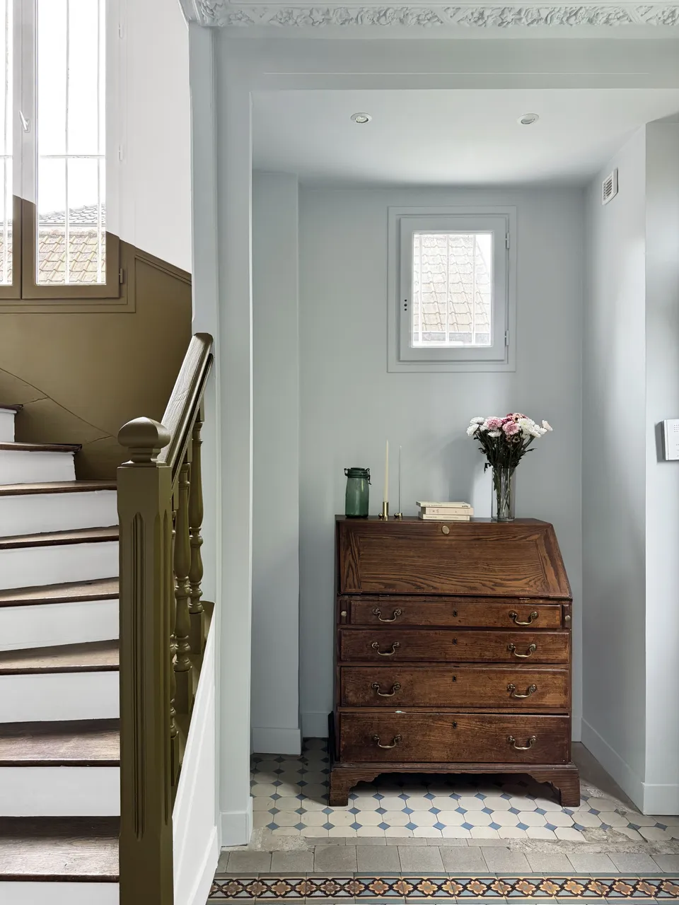 Studio Madame : architecte d’intérieur, Paris et Enghien-les-Bains.
Projet réalisé à Deuil-la-Barre.
Photographie d’intérieur : entrée d'une ancienne meulière rénovée à Deuil-la-Barre avec escalier ancien, moulures, plafond sculpté et niche bleu pâle, secrétaire ancien, cage d’escalier blanche avec soubassement vert bronze et carreaux de ciment d’origine au sol.