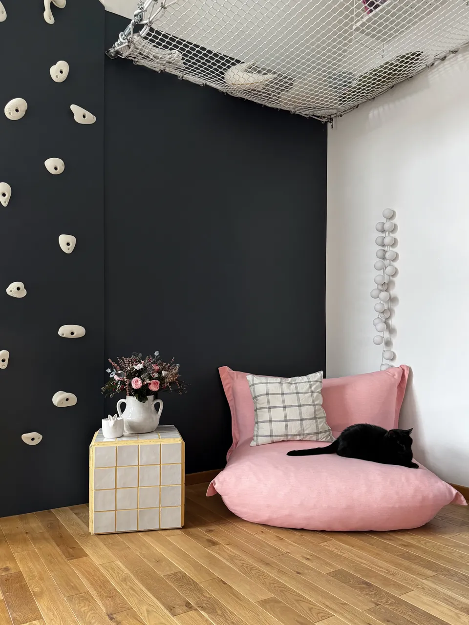 Studio Madame : architecte d’intérieur, Paris et Montmorency
Projet réalisé à Enghien-les-Bains.
Photographie d’intérieur : coin lecture composé d’un gros fauteuil bas rose bonbon, d’un petit guéridon à carreaux jaune et blanc, d’un bouquet de fleurs dans des tons de rose et de prises d’escalade blanches en béton permettant l’accès à un filet mezzanine suspendu en hauteur.