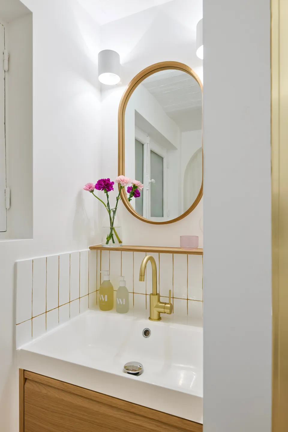 Studio Madame : architecte d’intérieur, Paris et Montmorency.
Projet réalisé à Deuil-la-Barre.
Photographie d’intérieur : petite salle de bain (vue sur coin vasque) composée d’un meuble vasque en chêne, d’une robinetterie dorée, d’une tablette/étagère et d’un miroir en chêne. Les murs sont peints en blanc (Ressource) et la vasque est entourée d’une faïence artisanale blanche avec des joints jaune ocre.