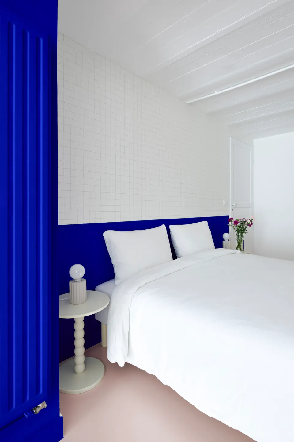 Studio Madame : architecte d’intérieur, Paris et Montmorency.
Projet réalisé à Deuil-la-Barre.
Photographie d’intérieur : arche et soubassement (tête de lit) peints en bleu Klein (Ressource), intégrant un espace nuit agrémenté d’un papier peint minimaliste quadrillé (Season Paper), d’une lampe et table de chevet beiges aux lignes originales et d’un lit avec parure blanche. Le plafond voûté est typique des sous-sols présents dans les meulières. Les murs sont peints en blanc et bleu Klein (Ressource) et le sol est habillé d’un béton ciré rose (Harmony Béton).