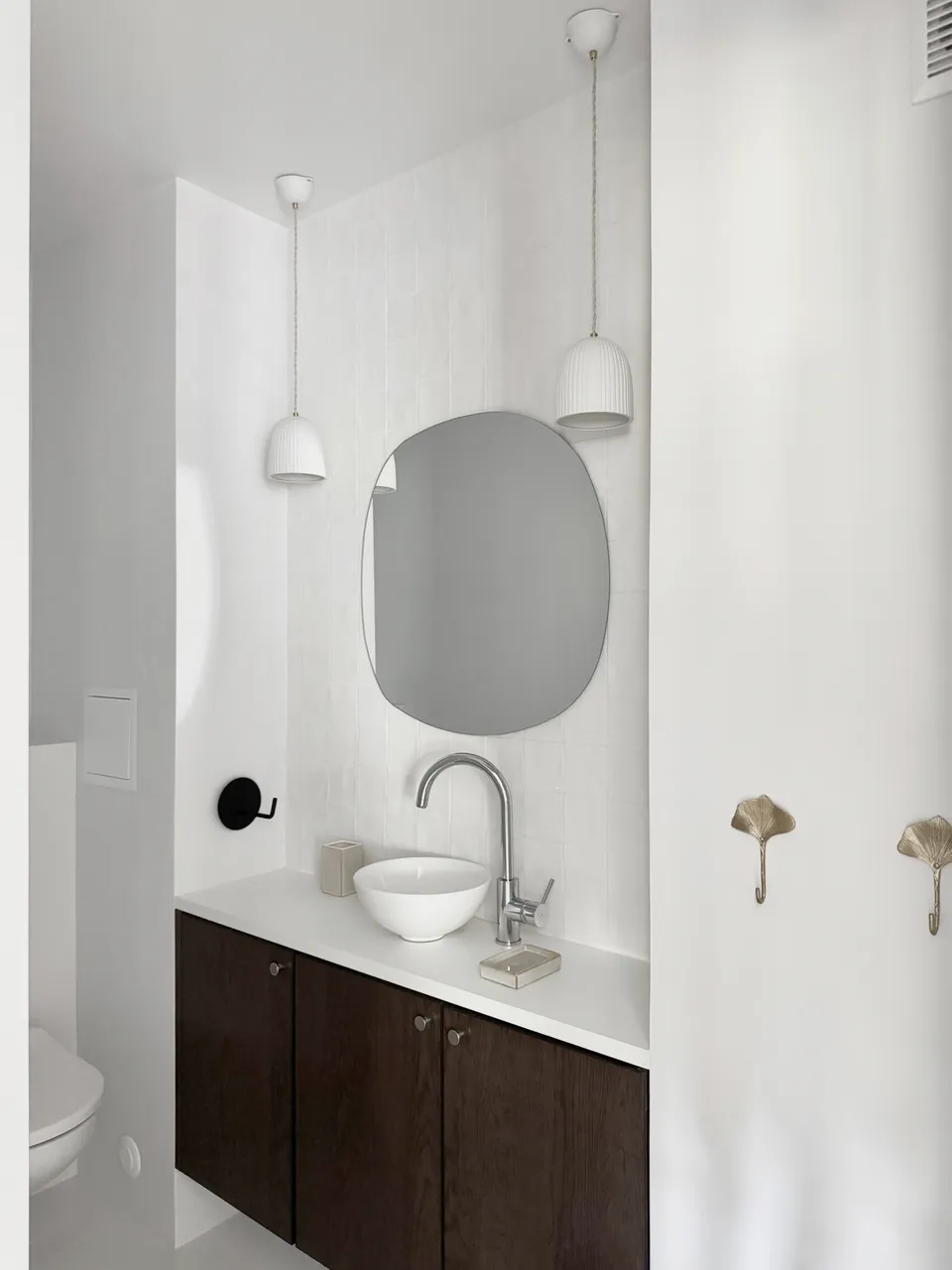 Studio Madame : architecte d’intérieur, Paris et Montmorency
Projet réalisé à Montmorency.
Photographie d’intérieur : salle de bain composée d’un meuble vasque avec plan de travail blanc, façades noyer et mitigeur chromé.
La salle de bain s’habille d’une faïence artisanale blanche sur l’un des murs et d’un béton ciré gris clair au sol.
Des suspensions en porcelaine tombent au-dessus du meuble vasque et autour du miroir.