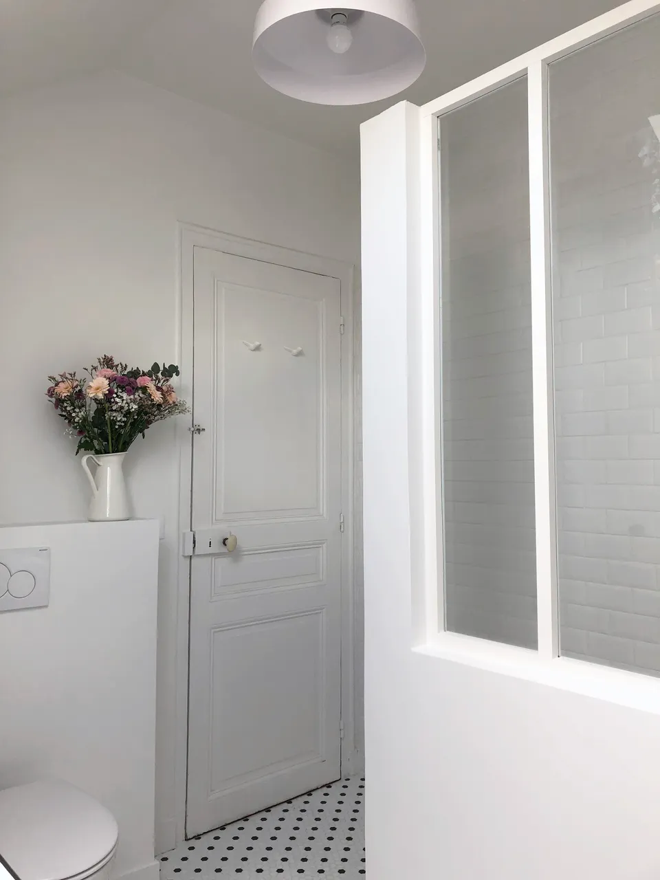 Studio Madame : architecte d’intérieur, Paris et Montmorency
Projet réalisé à Cormeilles-en-Parisis.
Photographie d’intérieur : salle de bain avec douche séparée par une verrière blanche, carreaux de métro en faïence, sol en mosaïque hexagonale blanche à pois noirs et patères en céramique en forme d’oiseau sur porte ancienne.