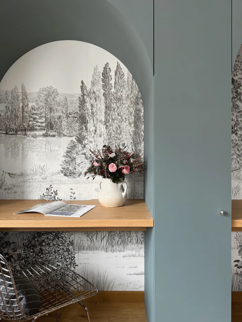 Studio Madame : architecte d’intérieur, Paris et Enghien-les-Bains
Projet réalisé à Enghien-les-Bains.
Photographie d’intérieur : aménagement sur mesure bleu de Nimes (Farrow & Ball) composé de colonnes et d’arches intégrant deux espaces bureau nichés entre les éléments. Un papier peint sous forme de fresque en noir et blanc tapisse le fond des niches.
Sur l’un des plateaux en chêne du bureau, un magazine ainsi qu’un bouquet de fleurs dans des tons de rose sont posés. Une chaise à quadrillage métallique est placée devant ce bureau.