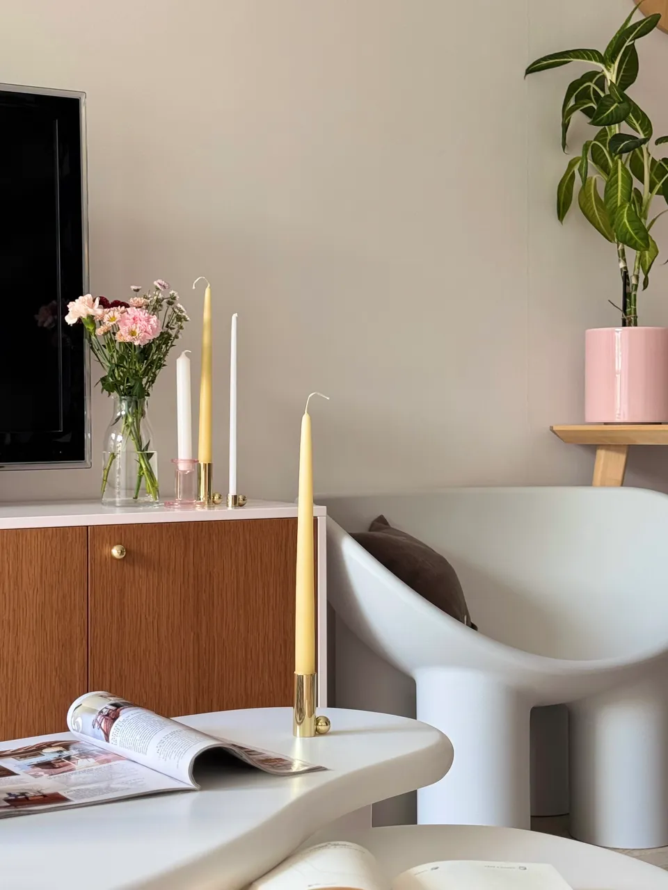 Studio Madame : architecte d’intérieur, Paris et Montmorency
Projet réalisé à Montmorency.
Photographie d’intérieur : salon composé d’un meuble TV rose et bois sur lequel reposent des bougeoirs, plusieurs bougies et un bouquet de fleurs. Un fauteuil blanc Roly Poly se tient juste à côté. Des tables basses asymétriques en ciment, sur lesquelles reposent un magazine, un carnet et une bougie, sont placées devant.