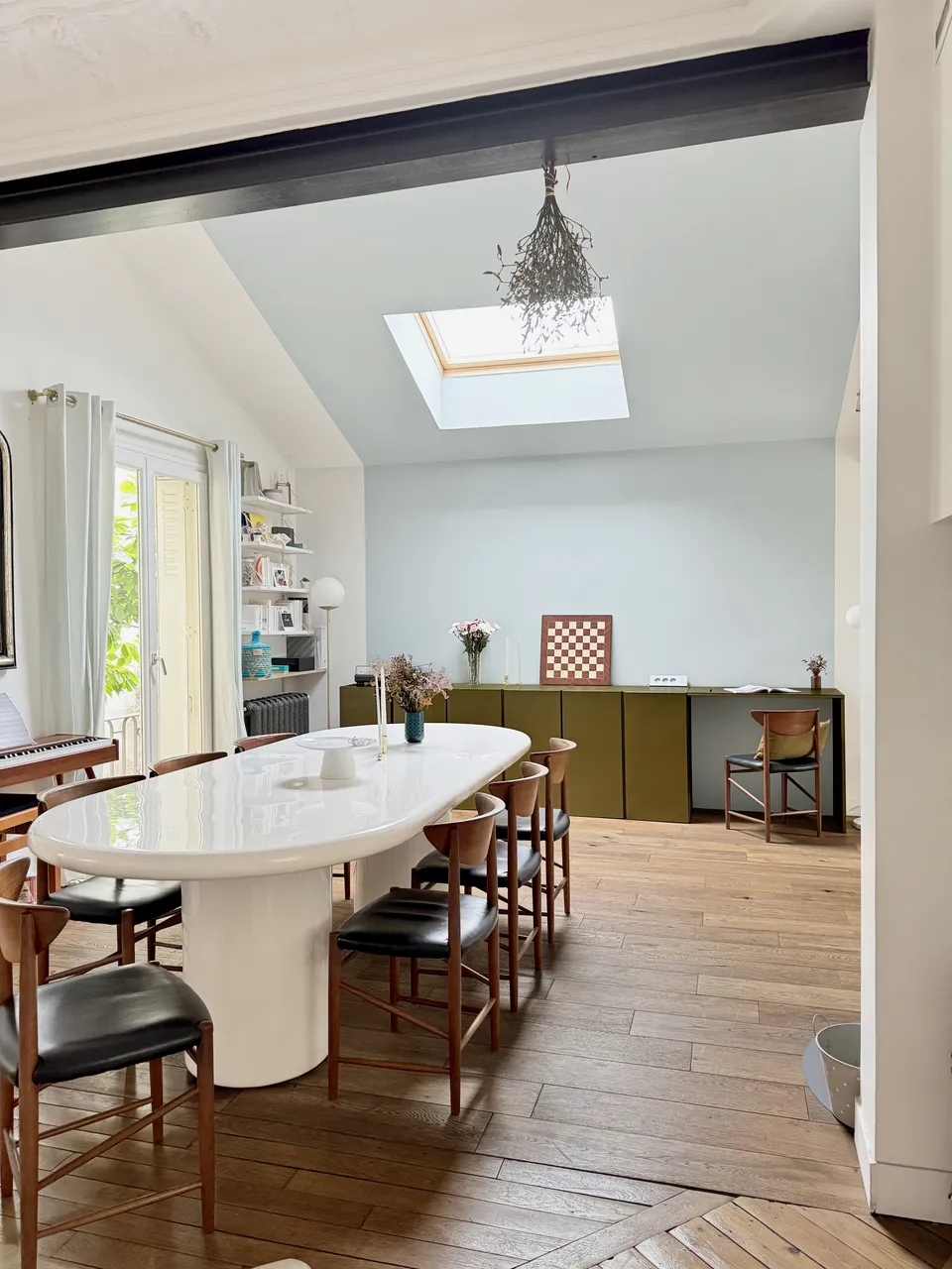 Studio Madame : architecte d’intérieur, Paris et Enghien-les-Bains.
Projet réalisé à Deuil-la-Barre.
Photographie d’intérieur : salle à manger d’une ancienne meulière rénovée à Deuil-la-Barre avec grande hauteur sous plafond, table en résine blanche et chaises design, incluant un bureau sur mesure vert bronze délimité par une alcôve formée par un mur et un plafond bleu pâle.