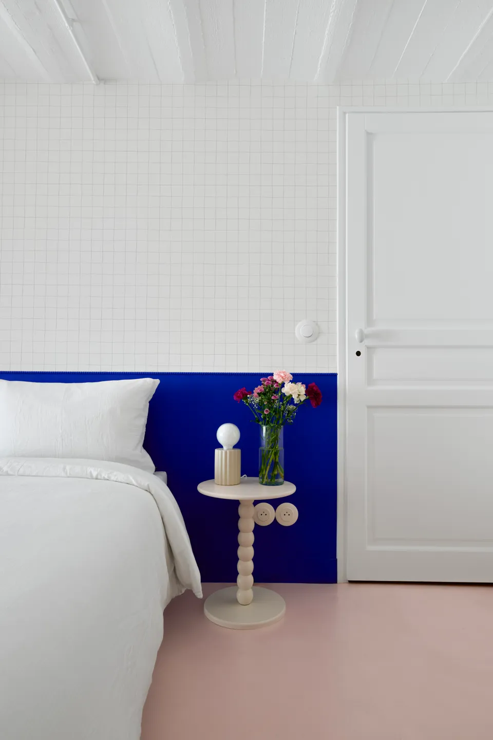 Studio Madame : architecte d’intérieur, Paris et Montmorency.
Projet réalisé à Deuil-la-Barre.
Photographie d’intérieur : soubassement (tête de lit) peint en bleu Klein (Ressource) intégrant un espace nuit agrémenté d’un papier peint minimaliste quadrillé (Season Paper), d’une lampe et table de chevet beiges aux lignes originales et d’un lit avec parure blanche. Le plafond voûté est typique des sous-sols présents dans les meulières. Les murs sont peints en blanc et bleu Klein (Ressource) et le sol est habillé d’un béton ciré rose (Harmony Béton).