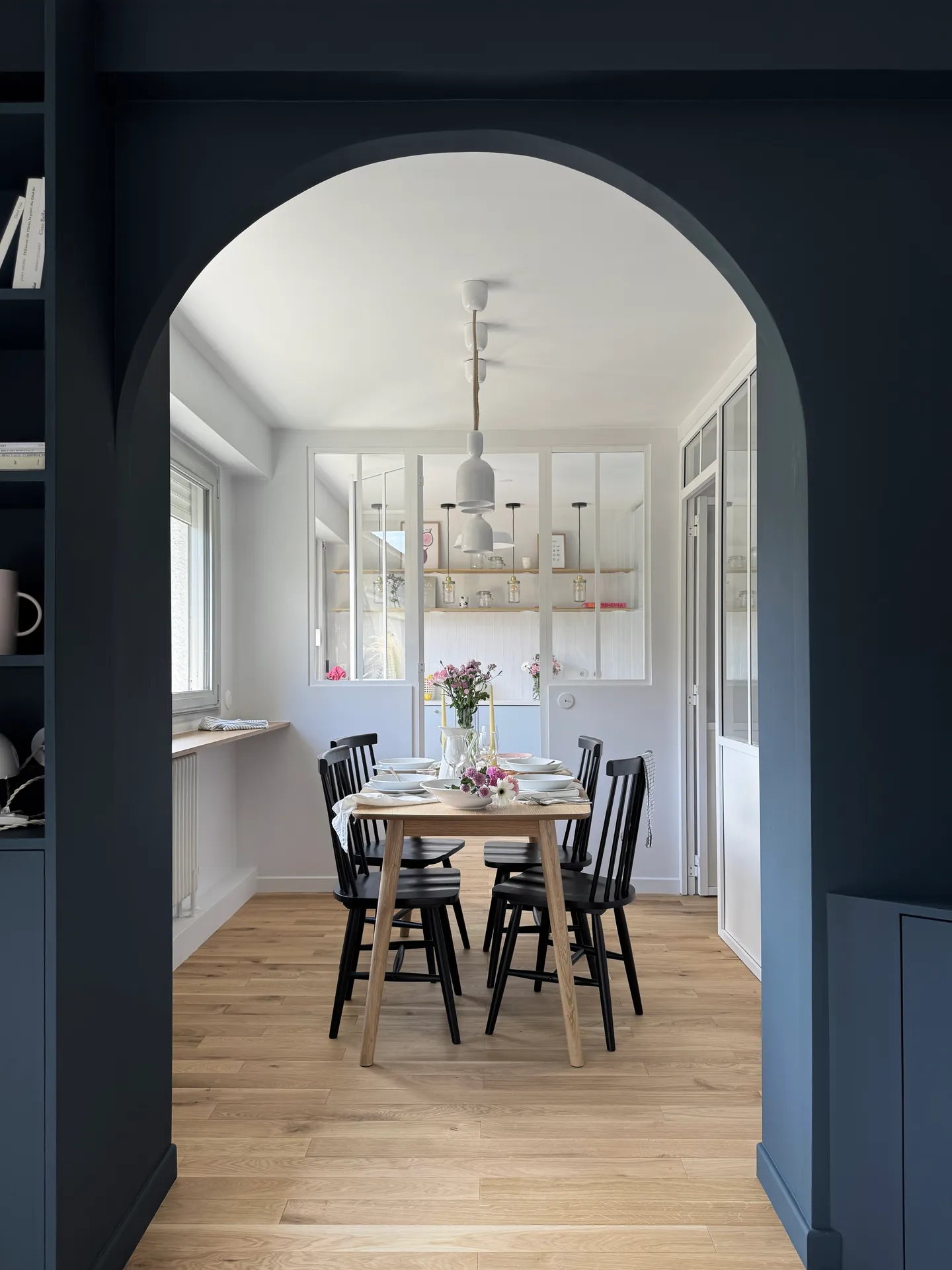 Studio Madame : architecte d’intérieur, Paris et Montmorency
Projet réalisé à Montmorency.
Photographie d’intérieur : salle à manger avec vue sur cuisine, composée d’une table rectangulaire avec 4 chaises vintages noires. La table est dressée et des suspensions tombent au-dessus de la table. La cuisine de couleur bleu ciel est visible en transparence grâce à la verrière atelier séparant les deux espaces.