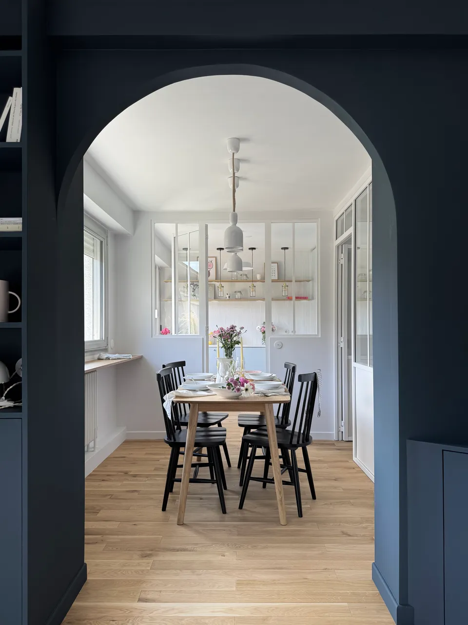 Studio Madame : architecte d’intérieur, Paris et Montmorency
Projet réalisé à Montmorency.
Photographie d’intérieur : salle à manger avec vue sur cuisine, composée d’une table rectangulaire avec 4 chaises vintages noires. La table est dressée et des suspensions tombent au-dessus de la table. La cuisine de couleur bleu ciel est visible en transparence grâce à la verrière atelier séparant les deux espaces.