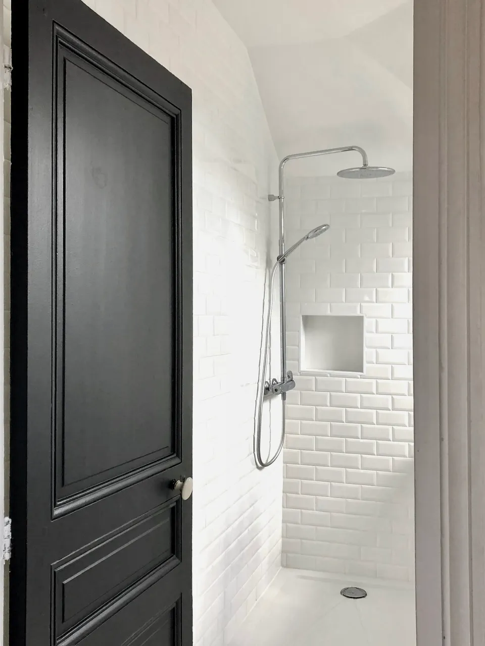 Studio Madame : architecte d’intérieur, Paris et Montmorency
Projet réalisé à Cormeilles-en-Parisis.
Photographie d’intérieur : salle de bain avec douche séparée par une verrière blanche, carreaux de métro en faïence, robinetterie chromée, niche carrée, et porte de salle de bain ancienne gris-bleu nuit.