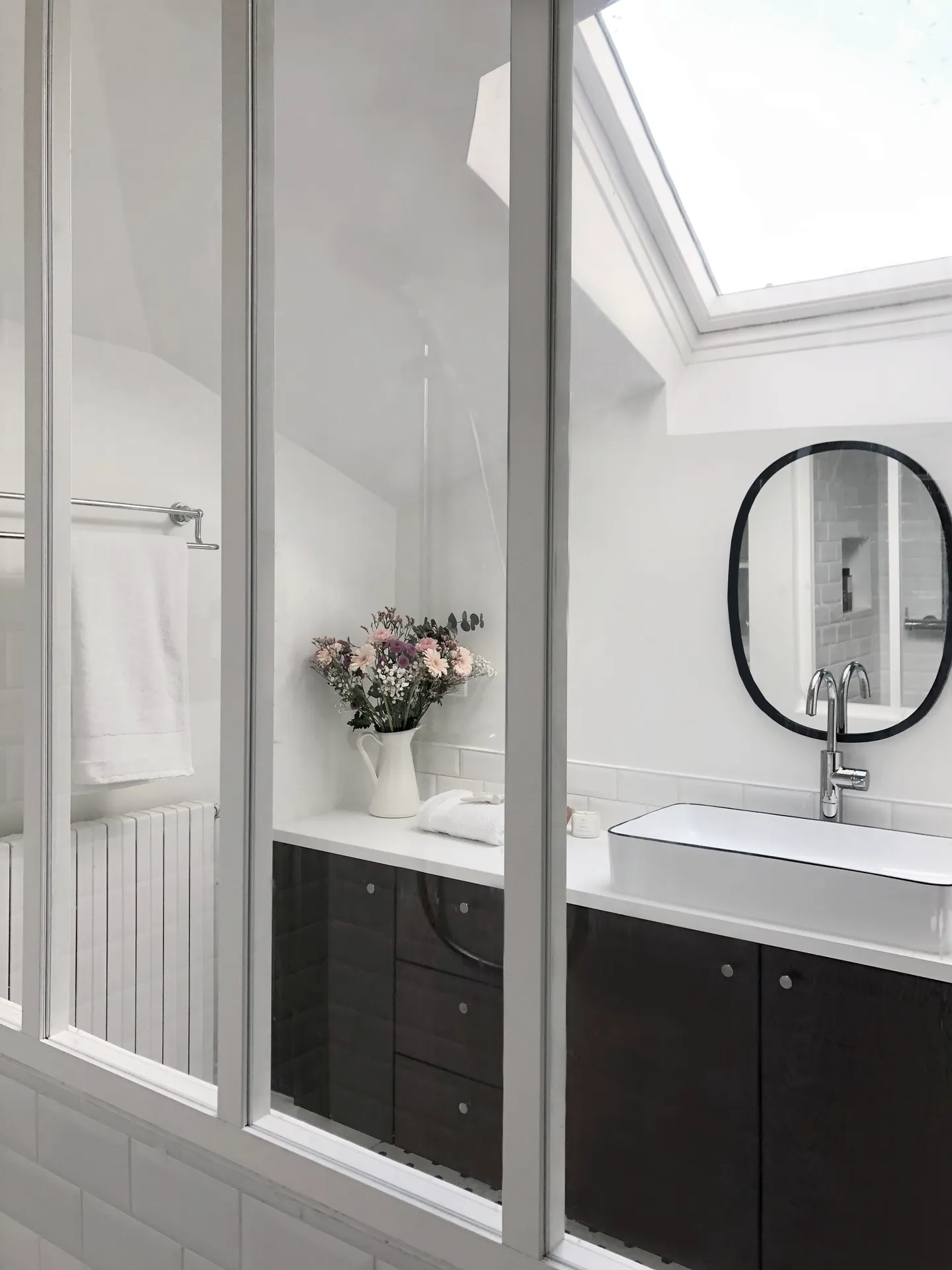 Studio Madame : architecte d’intérieur, Paris et Montmorency
Projet réalisé à Cormeilles-en-Parisis.
Photographie d’intérieur : salle de bain avec douche séparée par une verrière blanche, carreaux de métro en faïence, sol en mosaïque hexagonale blanche à pois noirs, meuble vasque en noyer et vasque en céramique, bouquet de fleurs dans des tons rose, blanc et mauve et porte-serviettes vintage chromé.