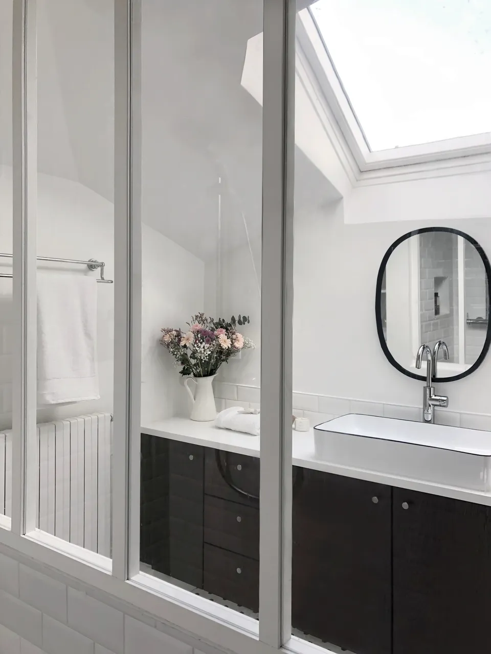 Studio Madame : architecte d’intérieur, Paris et Montmorency
Projet réalisé à Cormeilles-en-Parisis.
Photographie d’intérieur : salle de bain avec douche séparée par une verrière blanche, carreaux de métro en faïence, sol en mosaïque hexagonale blanche à pois noirs, meuble vasque en noyer et vasque en céramique, bouquet de fleurs dans des tons rose, blanc et mauve et porte-serviettes vintage chromé.