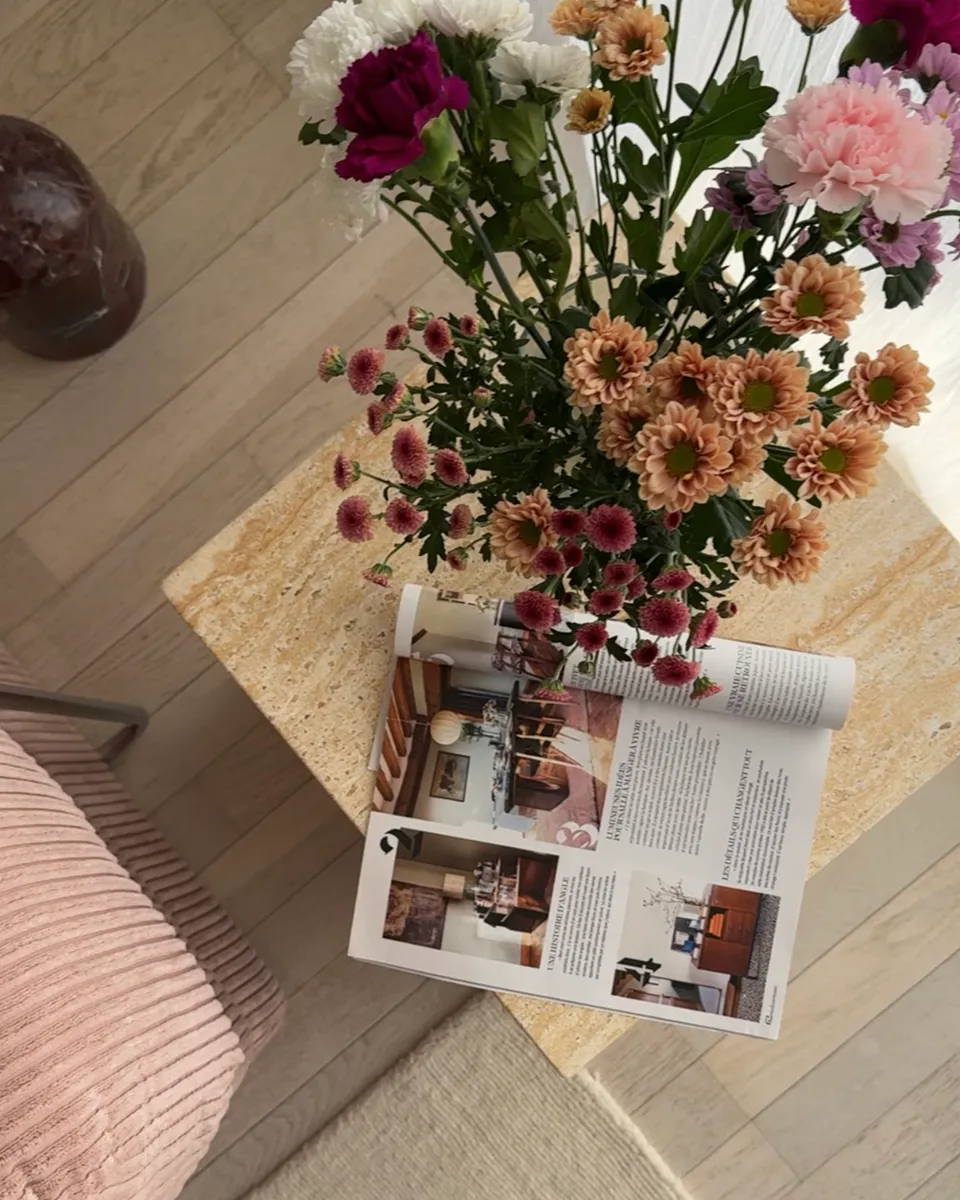 Studio Madame : architecte d’intérieur, Paris et Montmorency
Projet réalisé à Montmorency.
Photographie d’intérieur : salon composé d’un canapé rose, d’une lampe sur pied de couleur bordeaux, d’une petite table d’appoint en travertin sur laquelle reposent un bouquet de fleurs et un magazine de décoration.